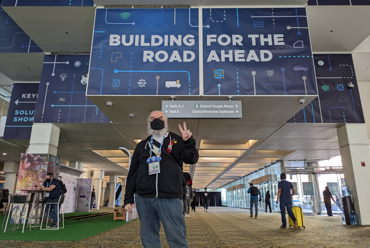 me standing in front of a kubecon banner